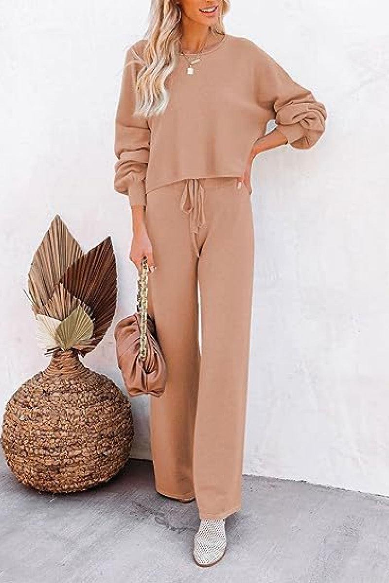 Woman wearing beige round neck loose fit cozy two-piece set with wide-leg pants and long sleeves, styled casually with a handbag and heeled shoes.