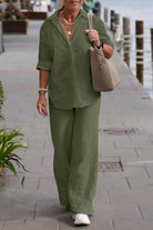 Woman wearing olive green relaxed shirt and trousers two-piece set with rolled sleeves and white shoes walking outdoors