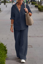 Woman wearing a navy relaxed shirt and trousers two-piece set walking on a city sidewalk carrying a beige woven bag