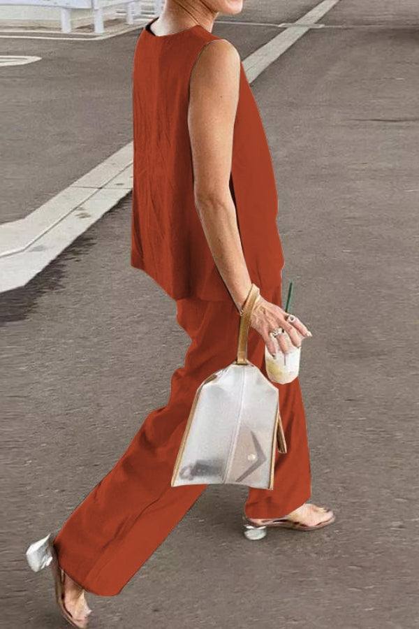 Woman wearing a loose solid color sleeveless two-piece set in rust with wide-leg pants and a transparent handbag walking outdoors