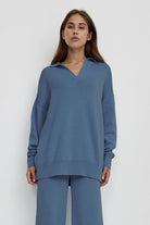 woman wearing plush and preppy camel two-piece set in blue with polo collar pullover and wide-leg pants against white background