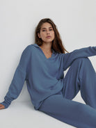 woman wearing plush and preppy camel two-piece set blue knit pullover and wide-leg pants seated on floor against white wall