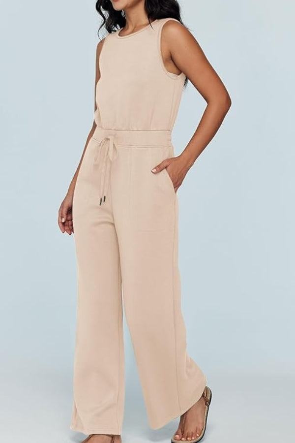 Woman wearing beige sleeveless wide leg pants jumpsuit with drawstring waist and pockets