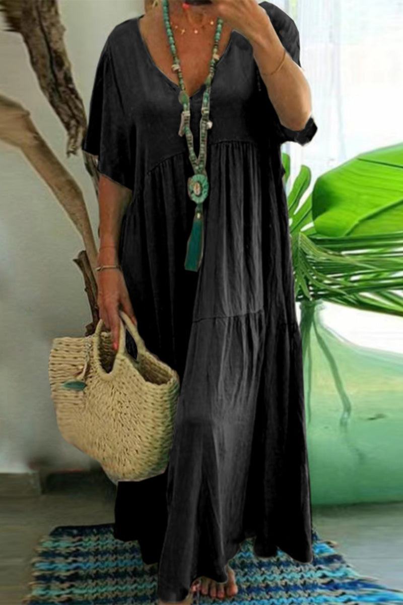 Black V-neck two-tiered maxi swing dress with flowing tiers and loose sleeves worn with a long necklace and woven handbag