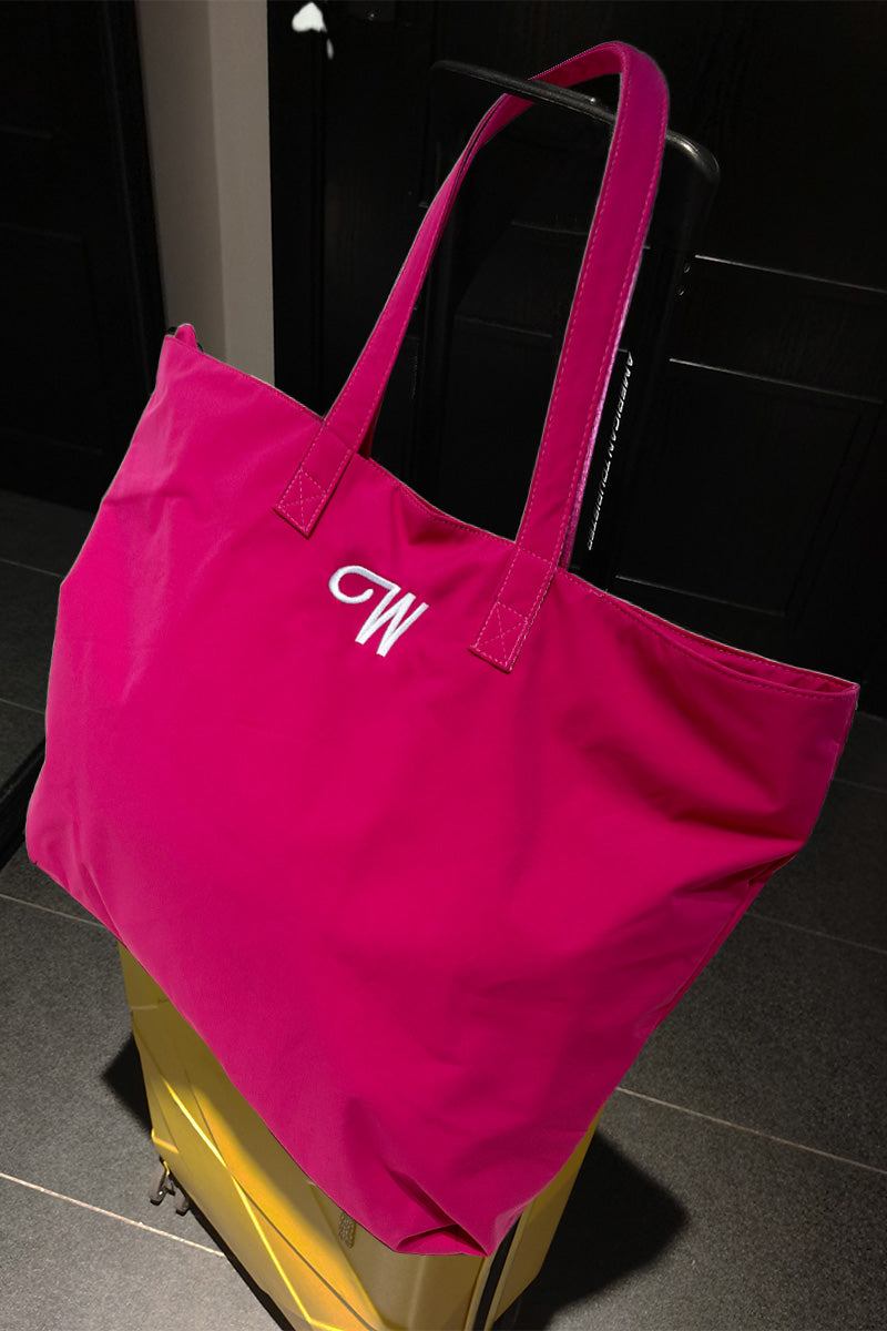 Bright pink waterproof travel bag with sturdy handles resting on yellow suitcase handle