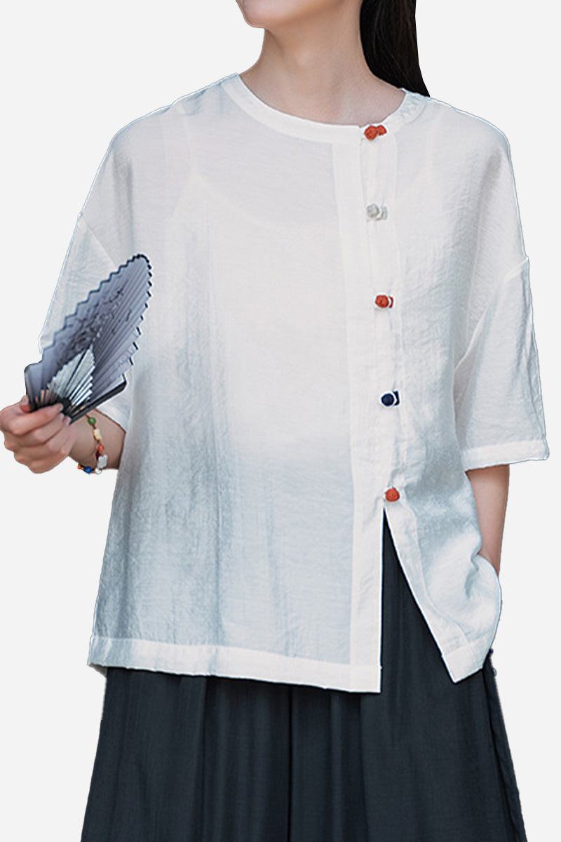 White regenerated cellulose blouse with asymmetrical colorful buttons and oversized fit worn by model holding a fan