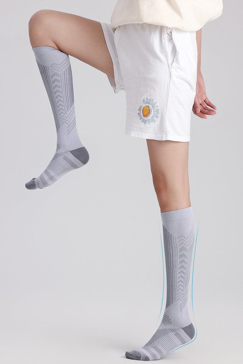 Light gray premium compression socks on a person wearing white shorts with a flower patch, designed for travel and leg comfort