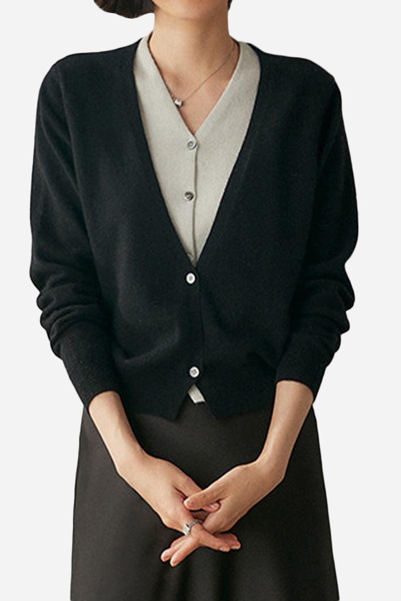 Woman wearing black single-breasted cashmere wool cardigan with V-neck and buttons over light gray top.
