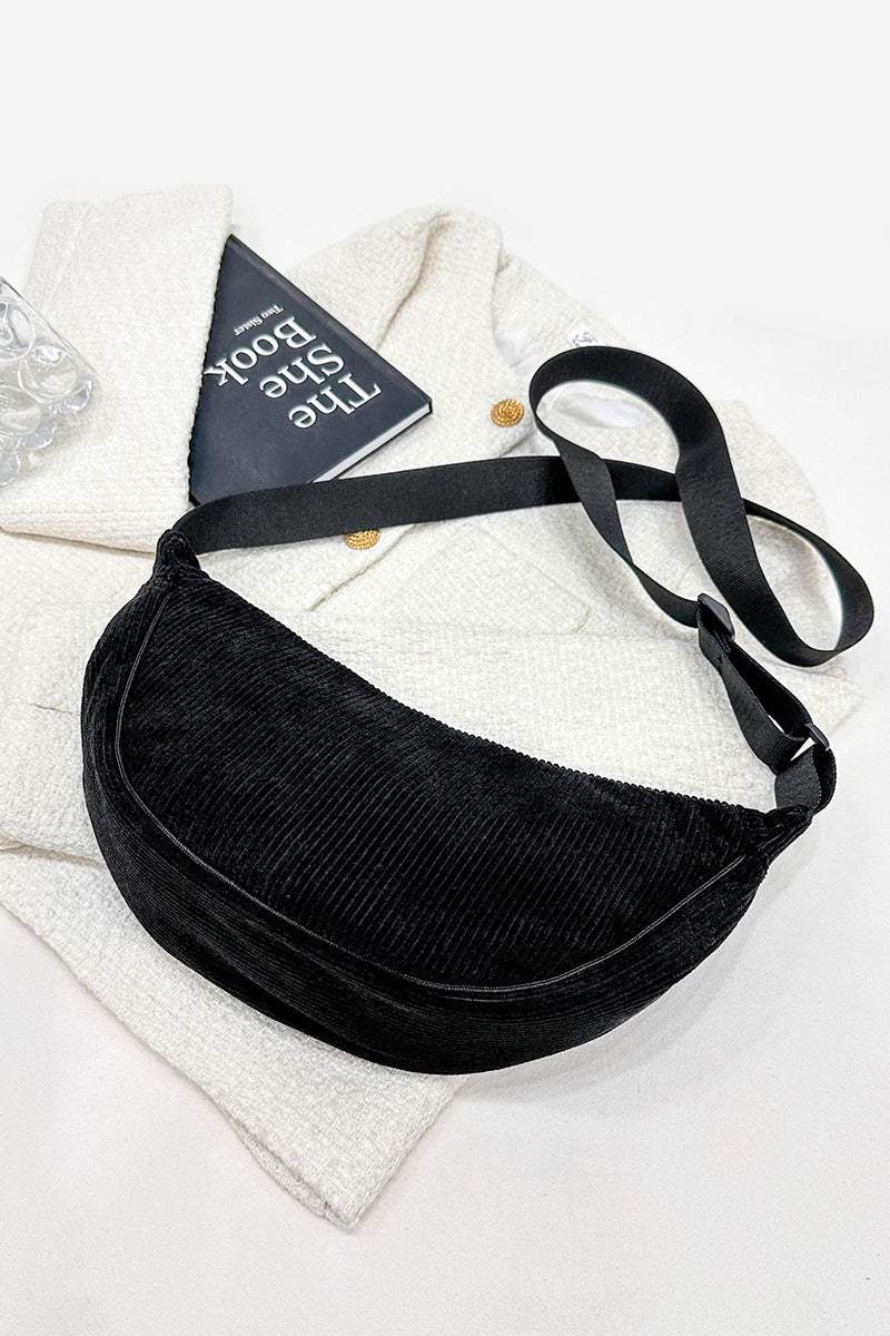 Black corduroy shoulder bag with adjustable strap on white textured fabric background