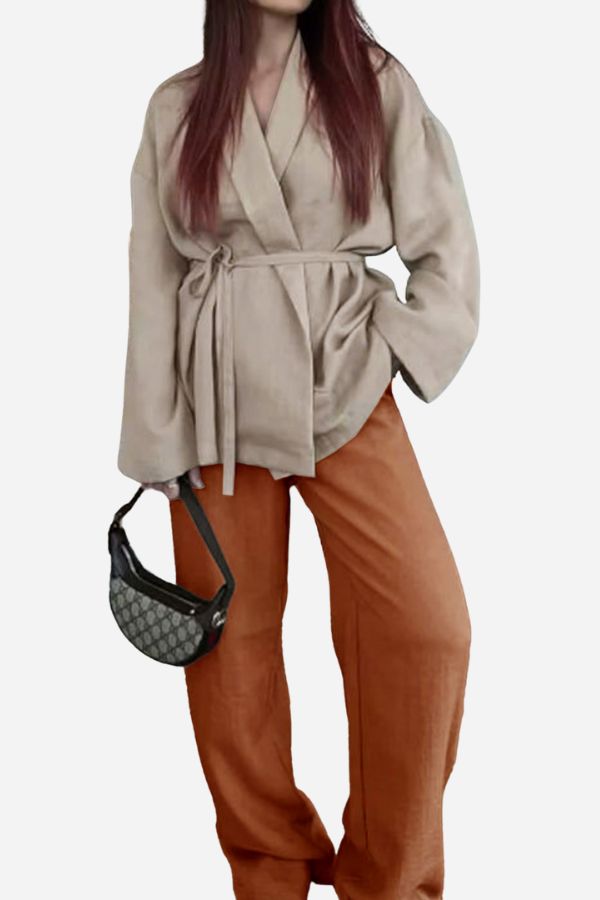 Woman wearing mix-match lounge-to-travel set with beige wrap top and rust-colored wide-leg pants holding a black handbag