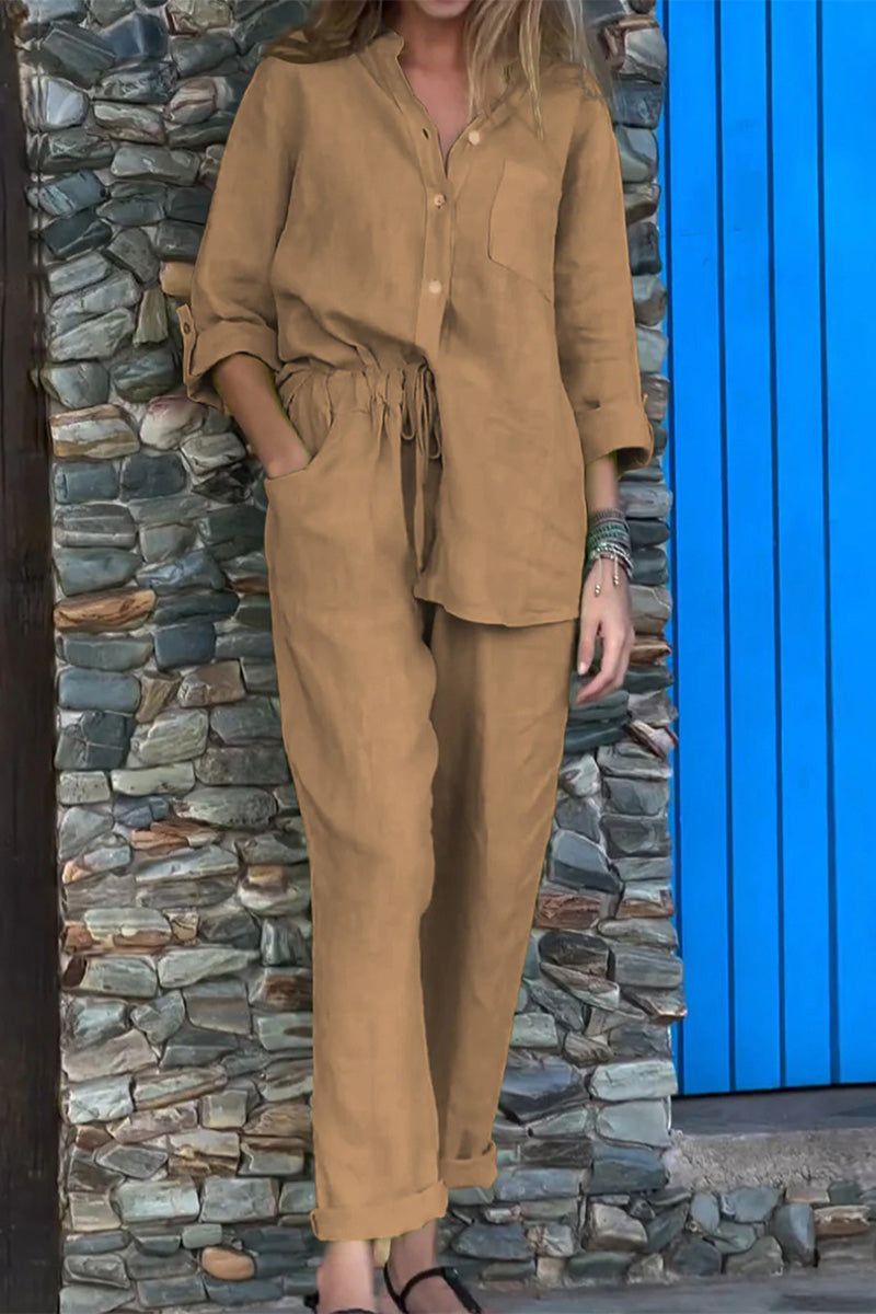 Woman wearing brown casual chic two-piece set with long sleeves and relaxed pants standing by stone wall and blue door