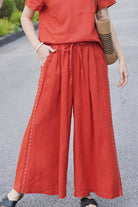 Women wearing wide-leg 100% linen pants in burnt orange with side stitch details and elastic waist, styled with matching top and casual sandals.