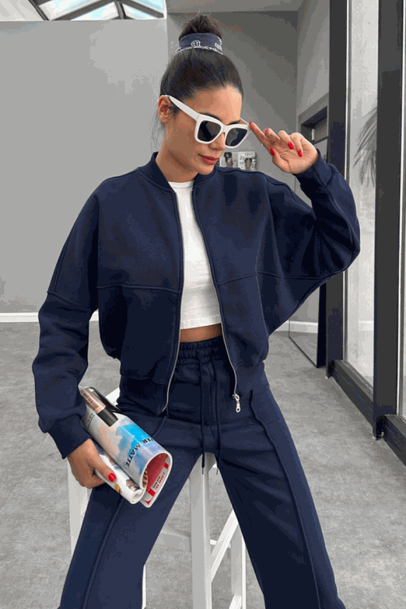 Woman wearing The Voyager Zip Set navy zip-front sweatshirt and wide-leg joggers with pockets, styled with white crop top and sunglasses.