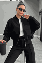 Woman wearing The Voyager Zip Set black zip-front sweatshirt and wide-leg joggers holding a cup, styled for travel and casual comfort.