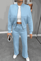 Woman wearing The Voyager Zip Set in light blue, featuring a zip-front sweatshirt and wide-leg joggers with pockets, styled with white sneakers and a white cropped top.