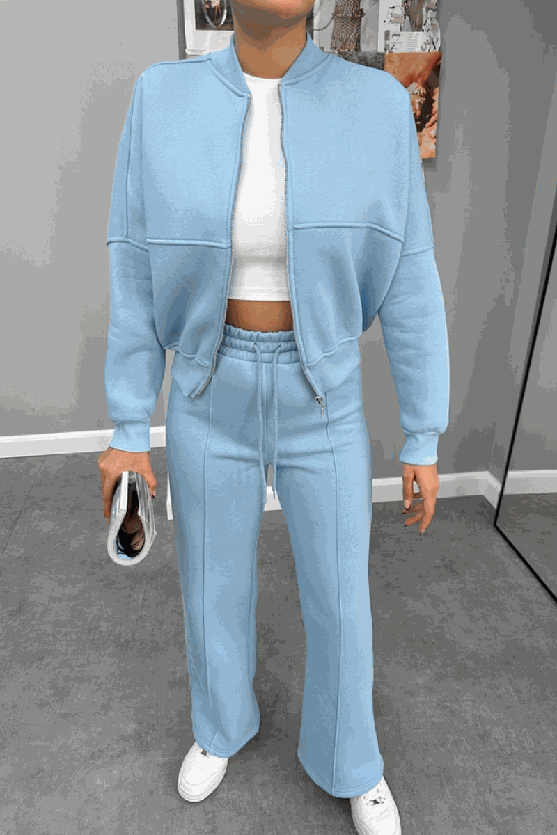 Woman wearing The Voyager Zip Set in light blue, featuring a zip-front sweatshirt and wide-leg joggers with pockets, styled with white sneakers and a white cropped top.