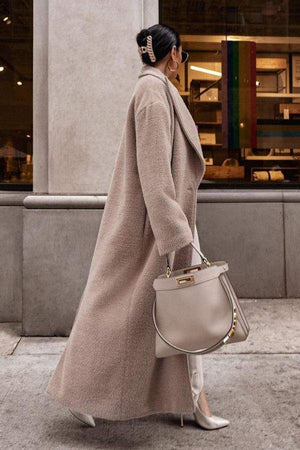 Woman wearing beige oversized teddy coat with ankle length and carrying beige handbag on city street