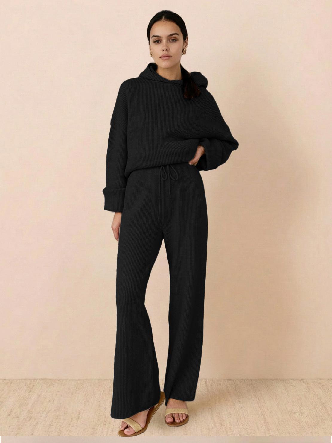 woman wearing black waffle-knit two-piece hoodie and pants set standing on beige floor against plain wall