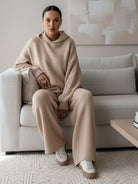 woman wearing beige waffle-knit two-piece hoodie and wide-leg pants sitting on couch indoors