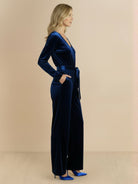 Woman wearing a deep V-neck velvet suit with long sleeves, removable waist tie, and wide-leg pants against a white background