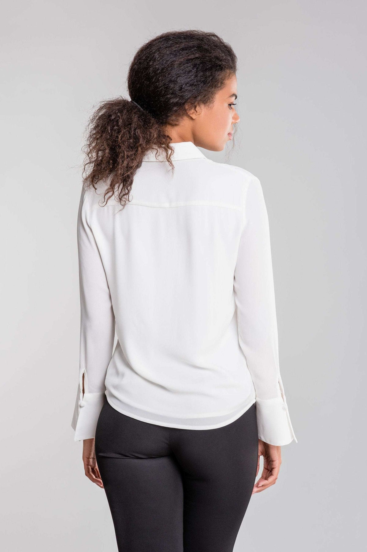 Back view of a woman wearing a white Bayam Blouse and black pants
