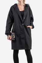Woman wearing black water resistant oversized hooded windbreaker jacket with buttons and elastic cuffs