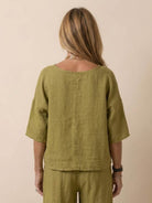 Back view of woman wearing olive green short-sleeved pullover and wide trouser matching set.