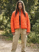 Woman wearing bright orange lightweight puffer travel jacket with beige cargo pants outdoors