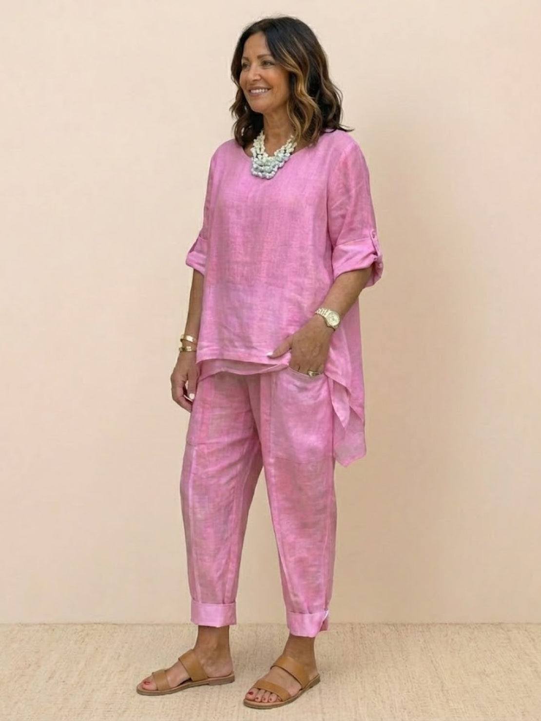 Woman wearing pink asymmetrical two-piece trouser set with rolled sleeves and cuffed pants standing against a beige background