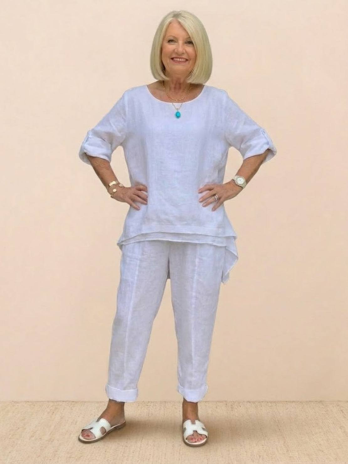 Older woman wearing white asymmetrical two-piece trouser set with rolled-up sleeves and tapered pants