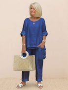 Woman wearing blue asymmetrical two-piece trouser set with rolled sleeves and holding a beige handbag.