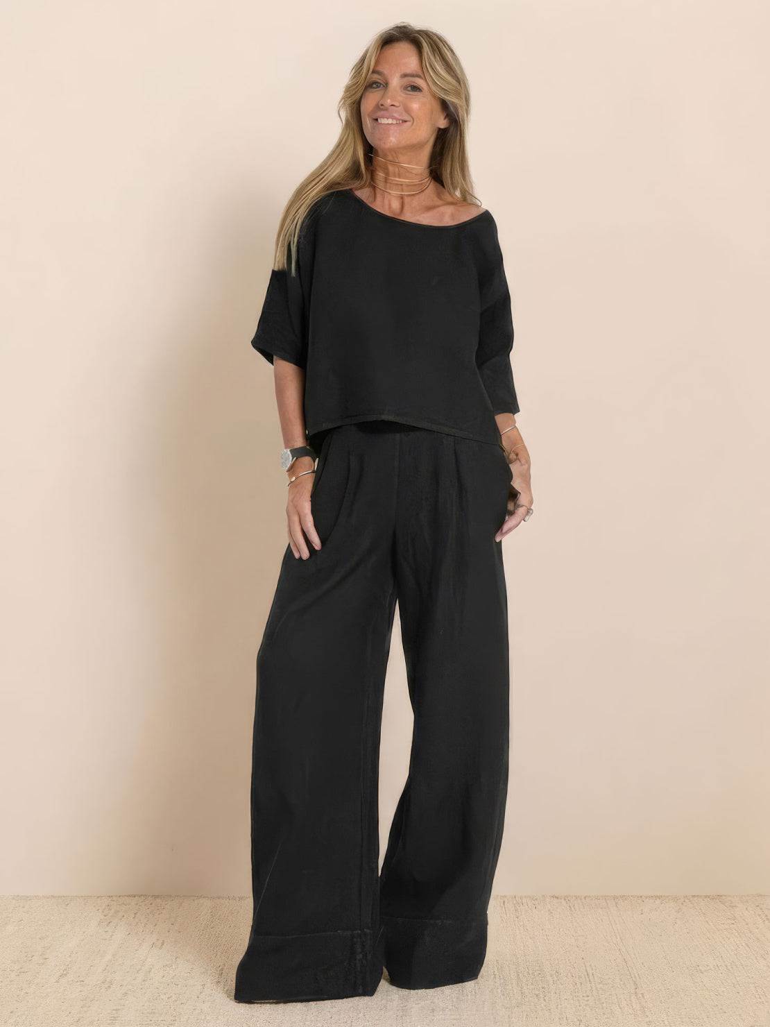 Woman wearing black short-sleeved pullover and wide trouser matching set against beige background