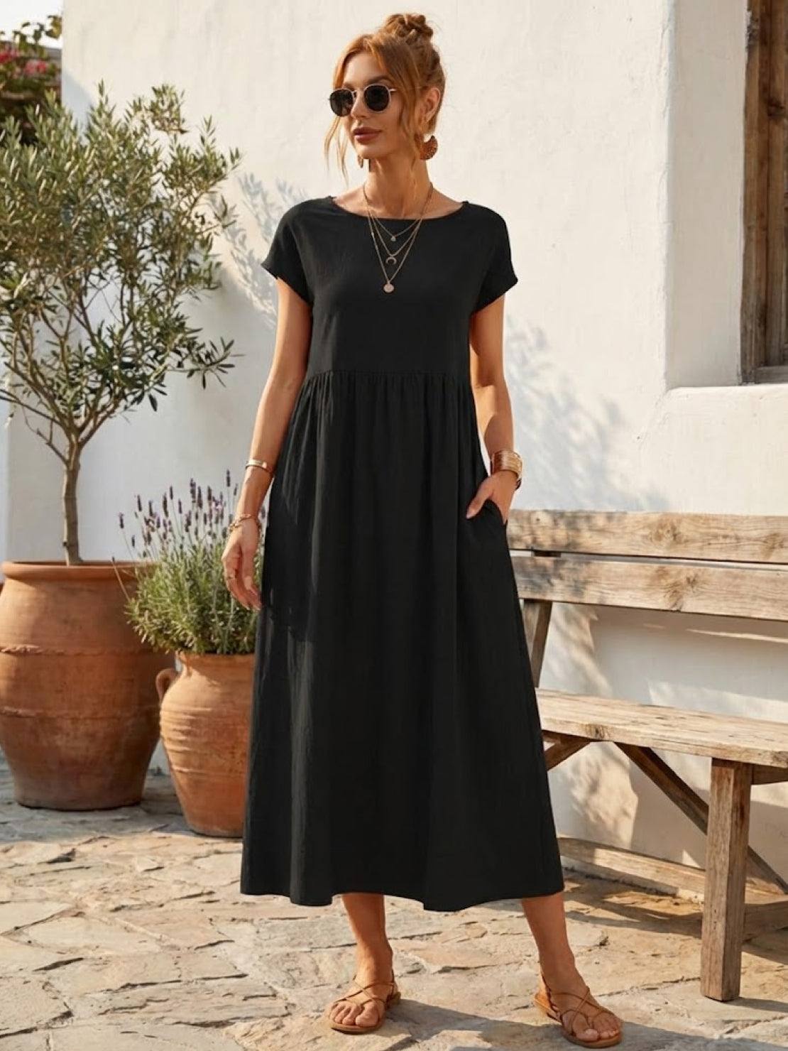 Woman wearing a capped-sleeve voluminous pleated midi dress with a flowing, stomach-flattening drape and pockets