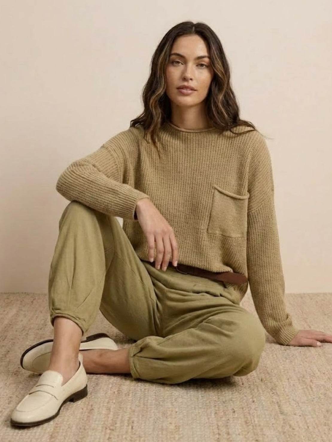 Woman wearing European Minimalism relaxed knit sweater and khaki trousers set sitting on floor
