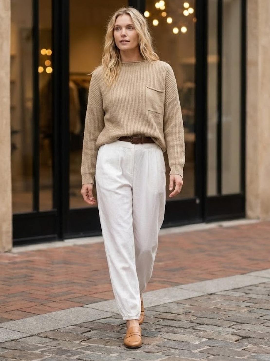 Woman wearing European minimalism relaxed knit sweater top and white trousers walking outdoors