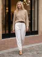 Woman wearing European minimalism relaxed knit sweater top and white trousers walking outdoors