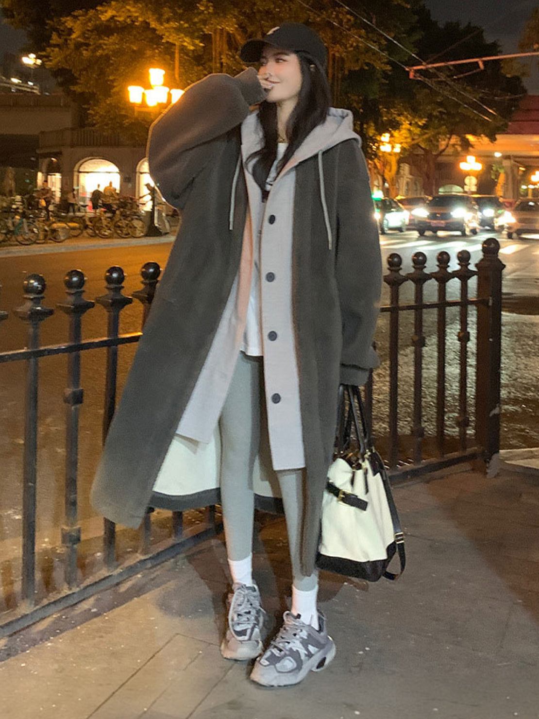 woman wearing everyday wear oversized sherpa long coat with cozy lining and casual sporty outfit on city street at night