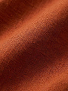 Close-up of soft, breathable loose solid color fabric in rust orange tone for two-piece set