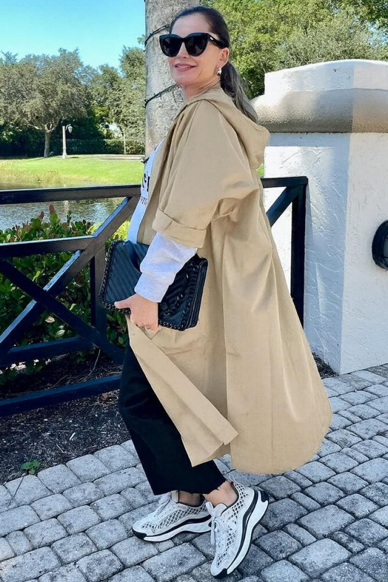 Woman wearing beige oversized water-resistant windbreaker jacket with hood and large pockets outdoors