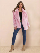 Woman wearing a pink open front oversized faux fur jacket with draped shawl collar, paired with black top, blue jeans, and beige boots.