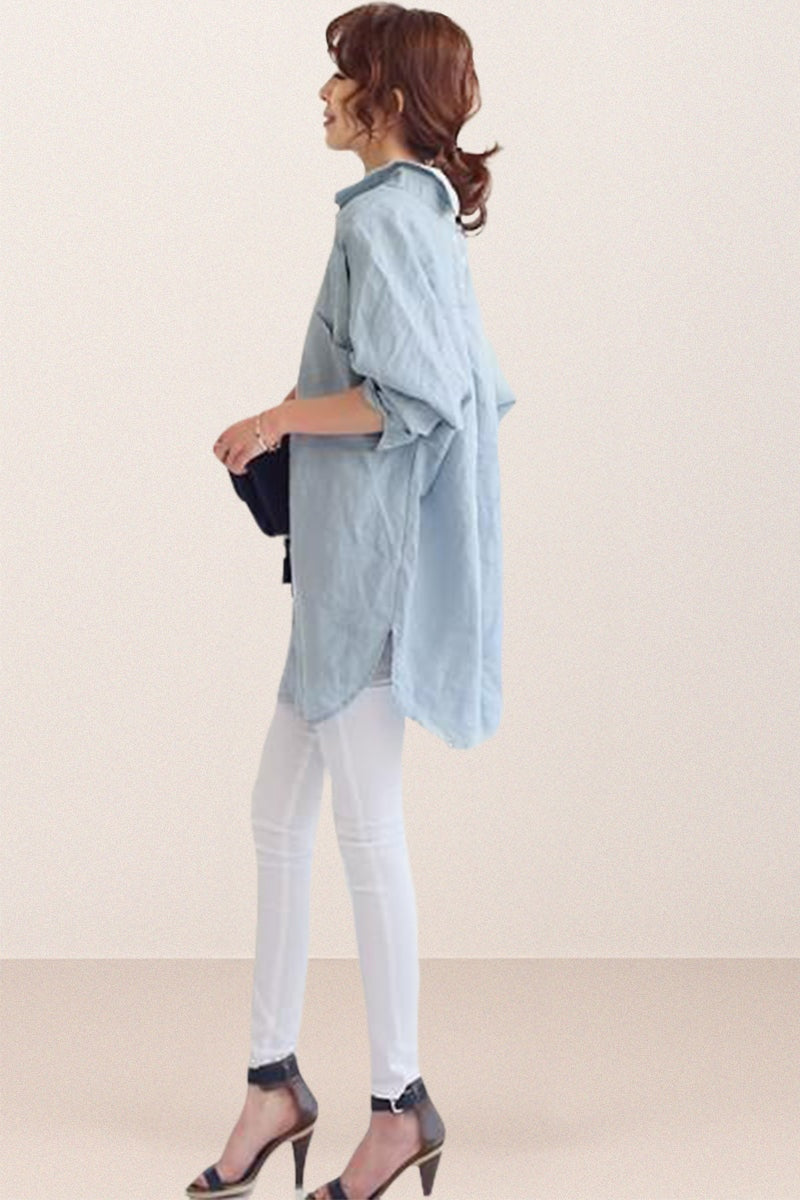 Woman wearing oversized light blue linen shirt with rolled-up sleeves and white pants