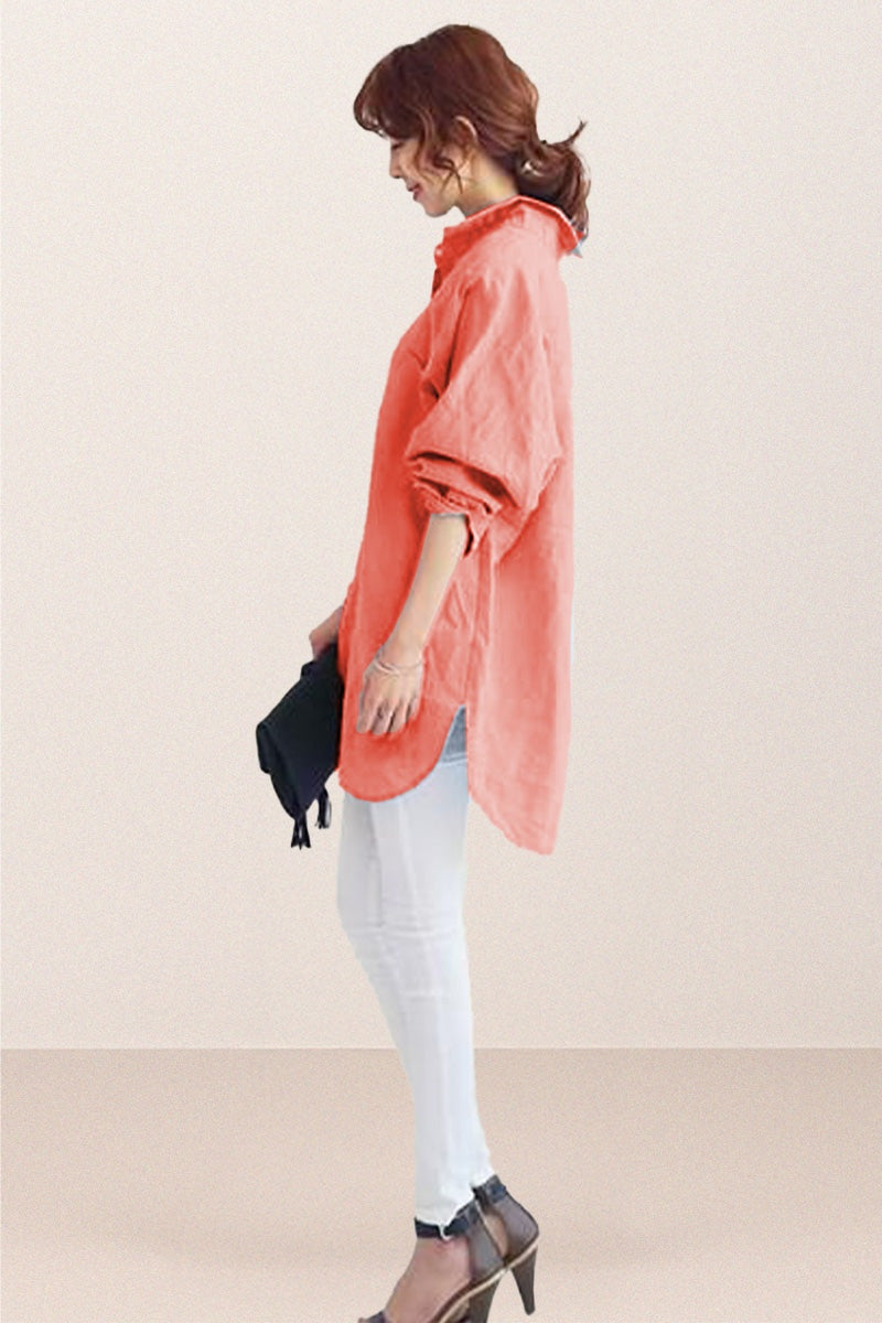 Woman wearing coral oversized linen shirt with rolled sleeves paired with white pants and heels, holding a black clutch.