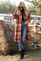 Woman wearing oversized medium-length plaid overshirt in shades of orange and brown, paired with jeans and black boots outdoors near hay bales