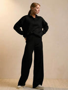 woman wearing plush and preppy camel two-piece set black outfit with polo collar and wide legs standing against beige background