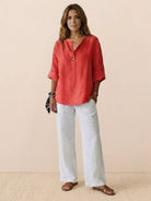 Woman wearing coral pure linen age-defying shirt with button detail and white linen pants