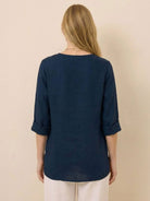 Back view of woman wearing navy blue pure linen age-defying button detail shirt with rolled sleeves