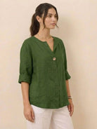 Woman wearing green pure linen age-defying button detail shirt with rolled sleeves and white pants