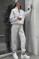Woman wearing white cotton blend tracksuit with zip neckline and sneakers, standing indoors