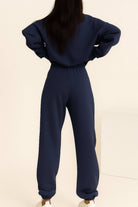 Woman wearing navy blue cotton blend tracksuit with long sleeves and elastic waist and cuffs, viewed from back.