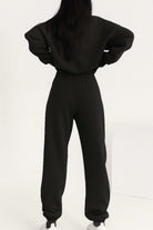 Back view of woman wearing black cotton blend tracksuit with stretch waistband and cuffs, showcasing relaxed fit and minimalist style.